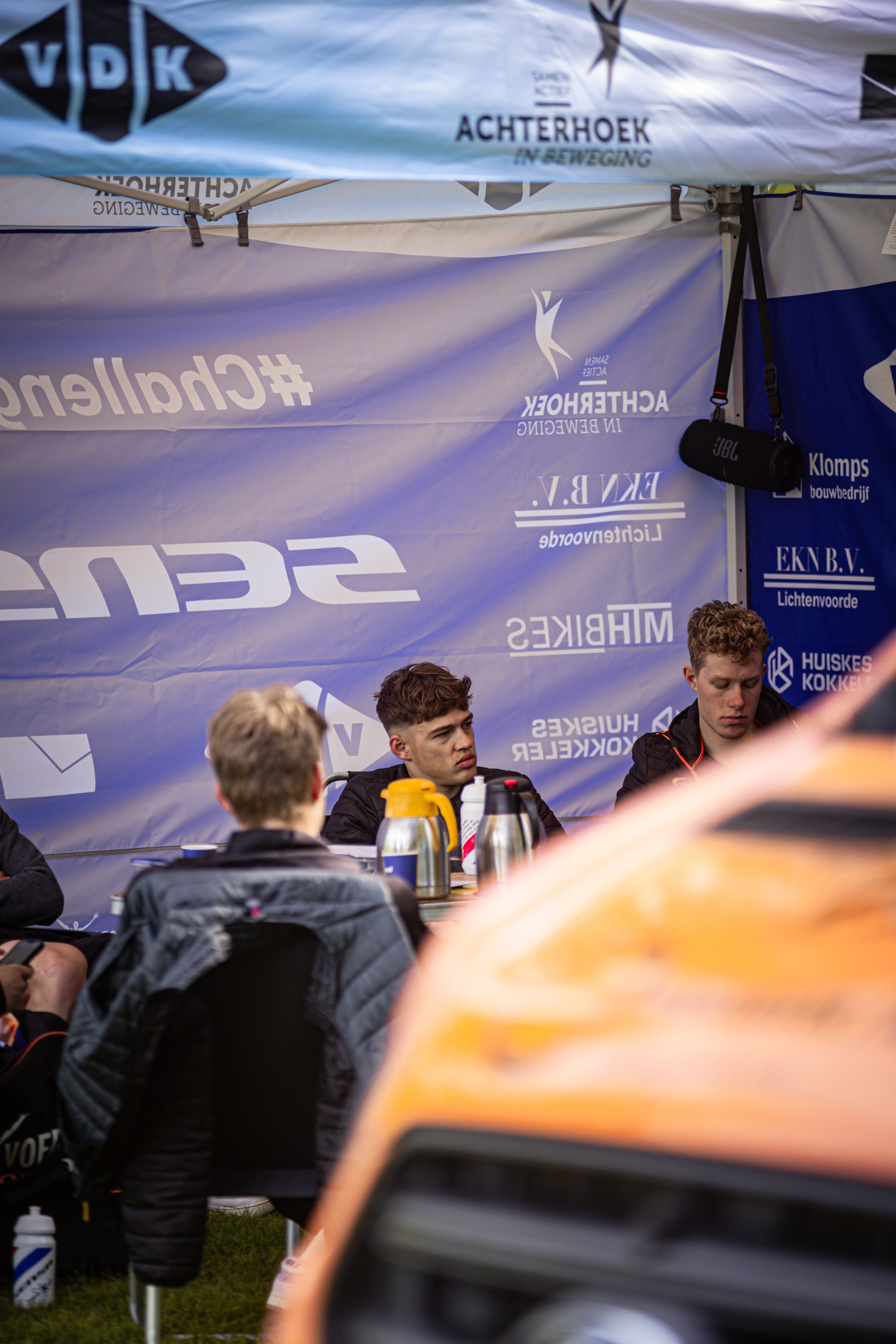 A group of men sitting in front of a blue banner for the Ronde Van Overijssel.