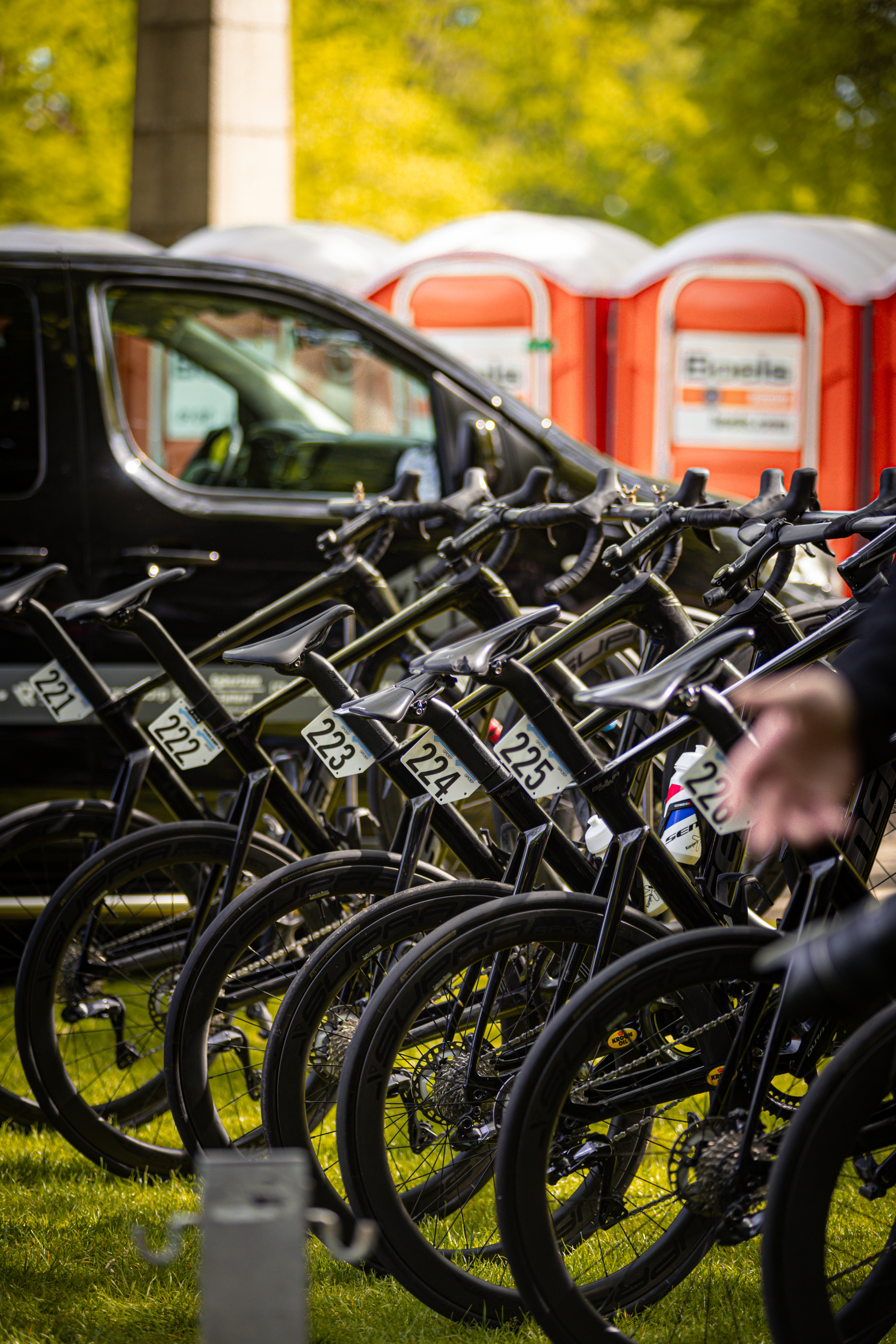 A group of bicycles sit in a row on the grass, with one labeled 2024 and another bearing the number 28.