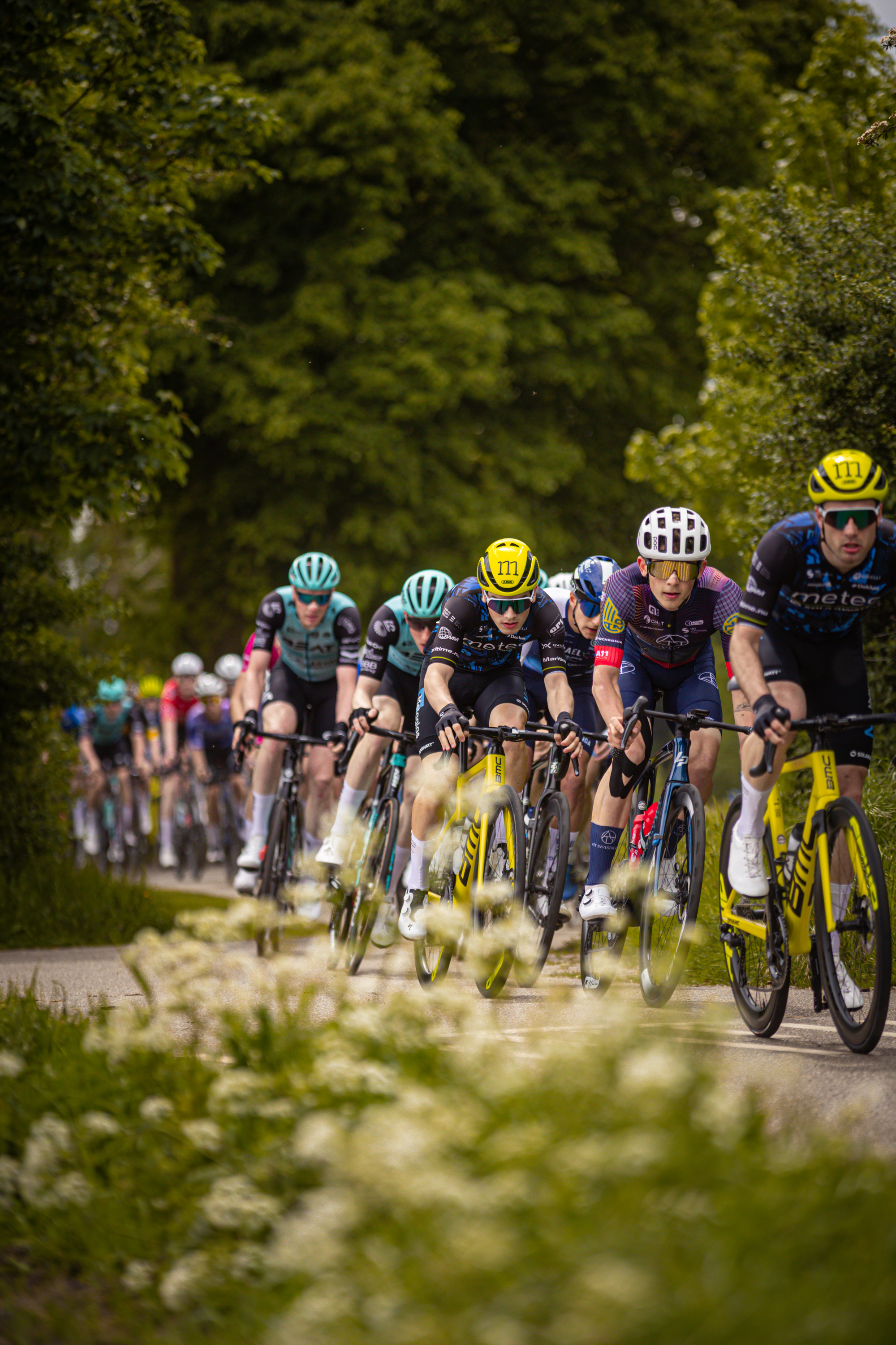 A group of cyclists wearing helmets race down a path.