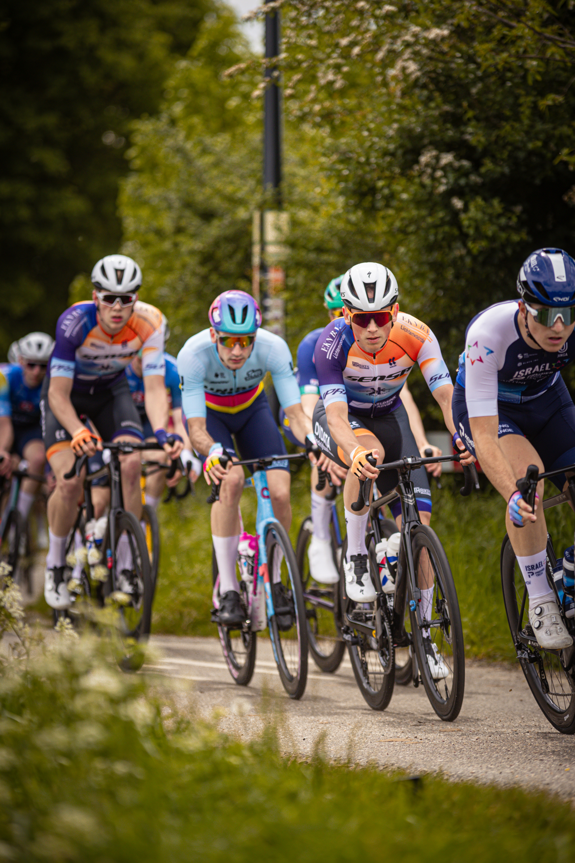 Four cyclists are wearing helmets, jerseys and riding bikes on the street.