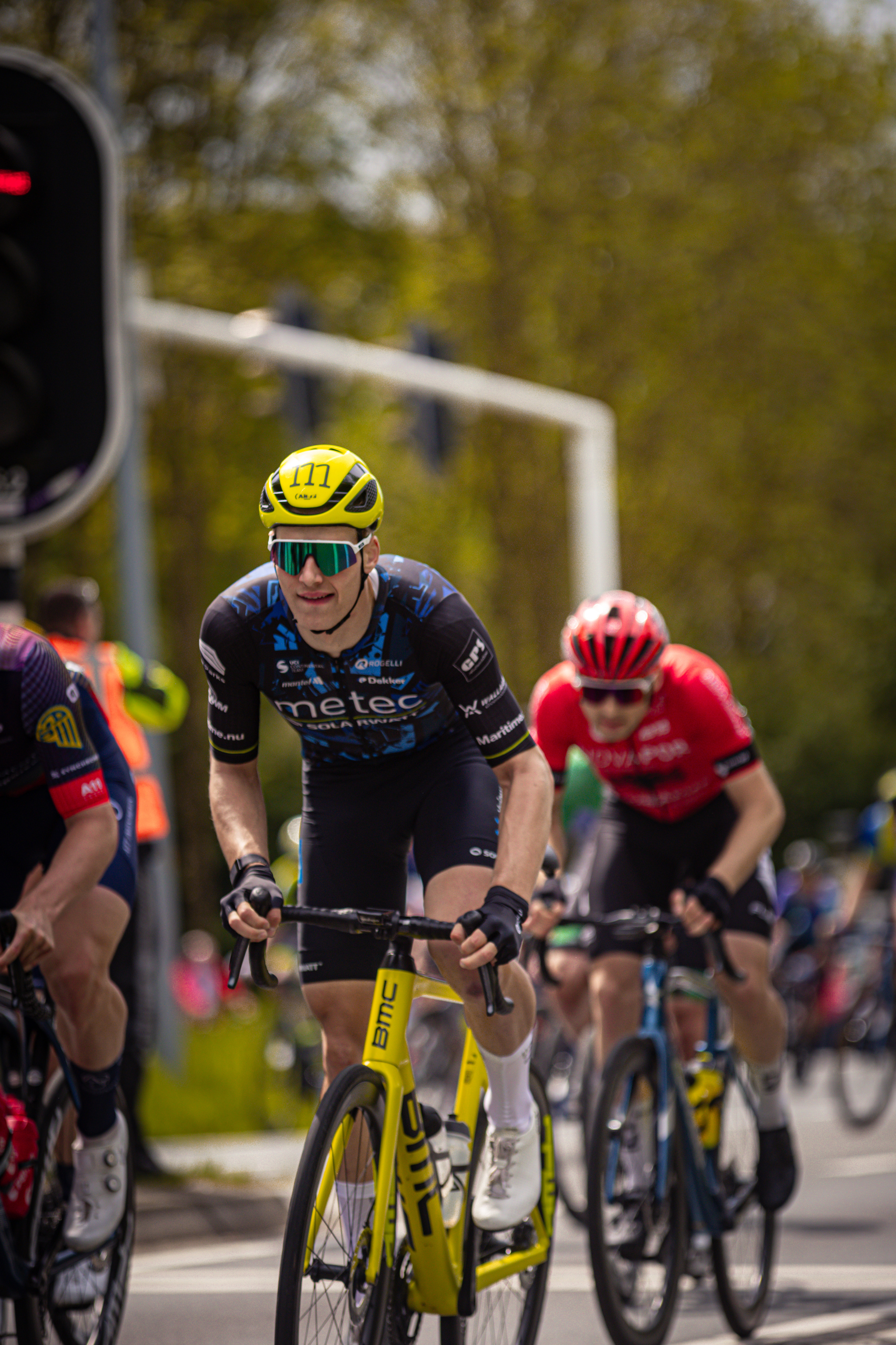 A cyclist wearing a yellow and black helmet is racing with other cyclists during the Rode van Overijssel.