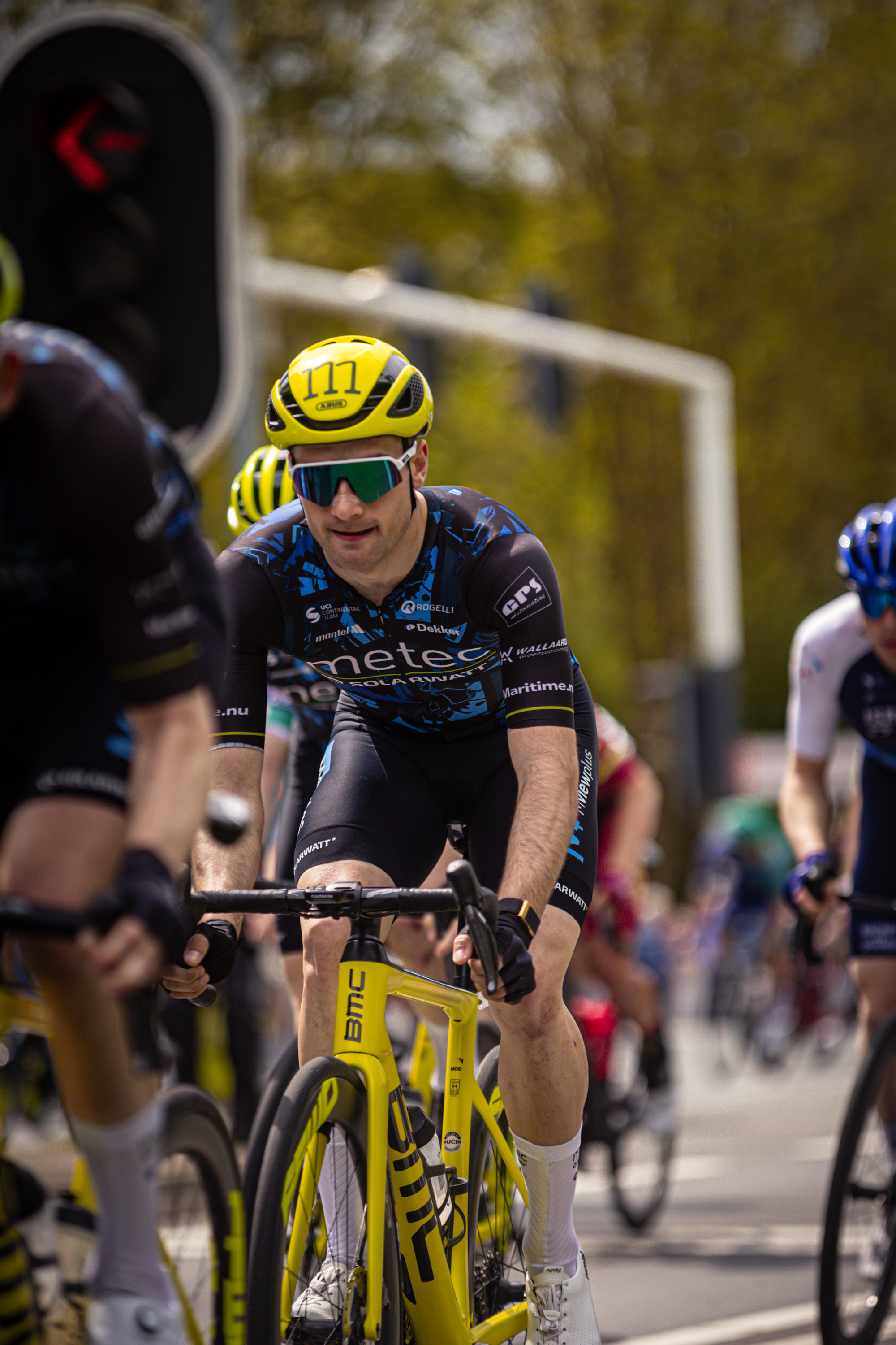 A group of cyclists wearing helmets race down a street.