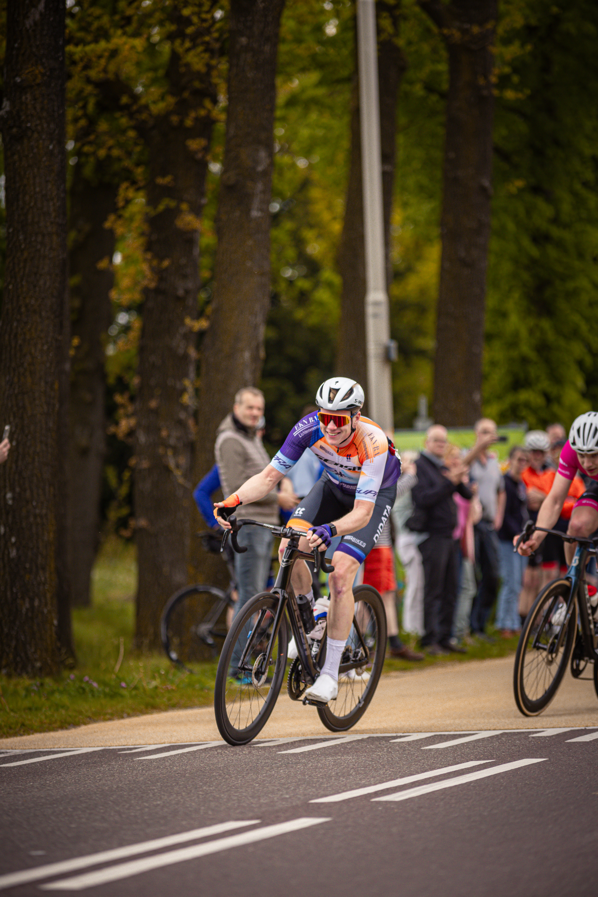 Two cyclists participating in a race and some people watching them.