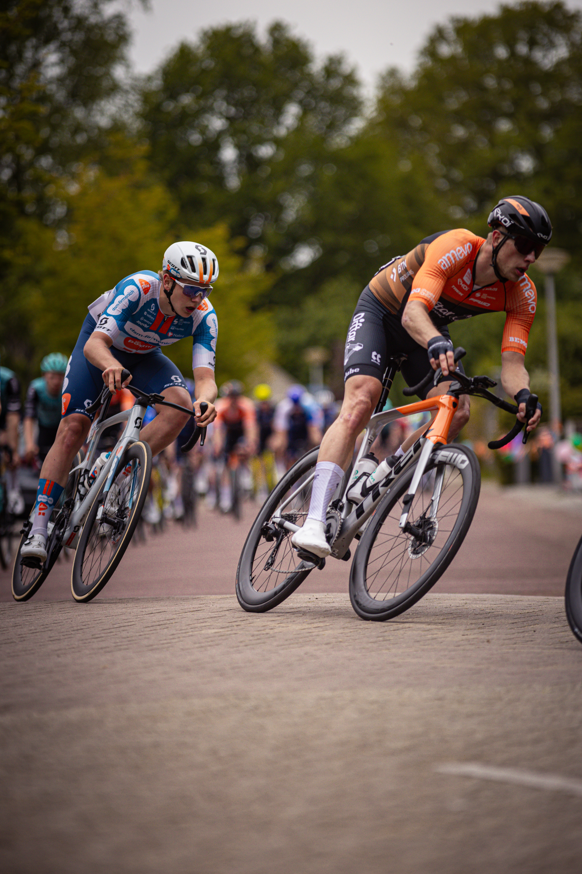 Two cyclists race down a track in the Netherlands, one of them wearing an orange jersey.