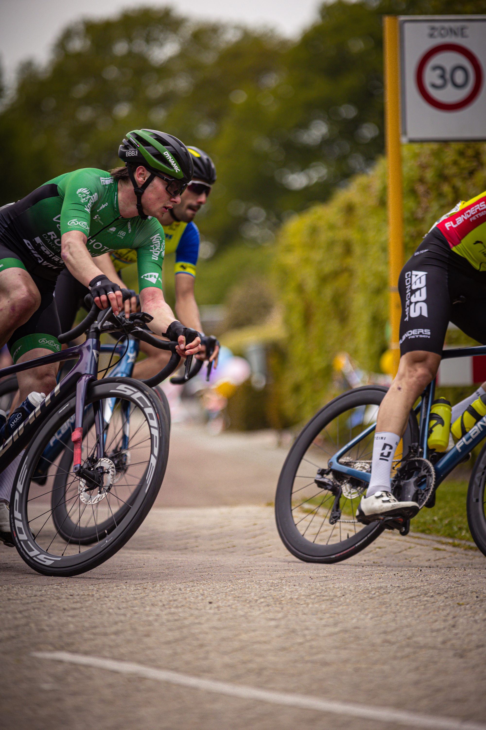 A cyclist in a green jersey is riding down a street with other cyclists.