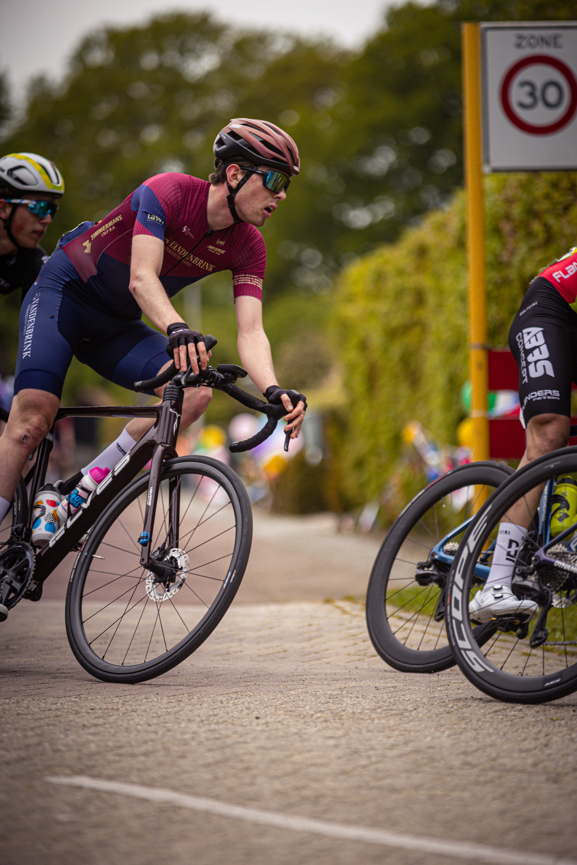 Three cyclists race along a path, one of them wearing a black number 30 jersey.