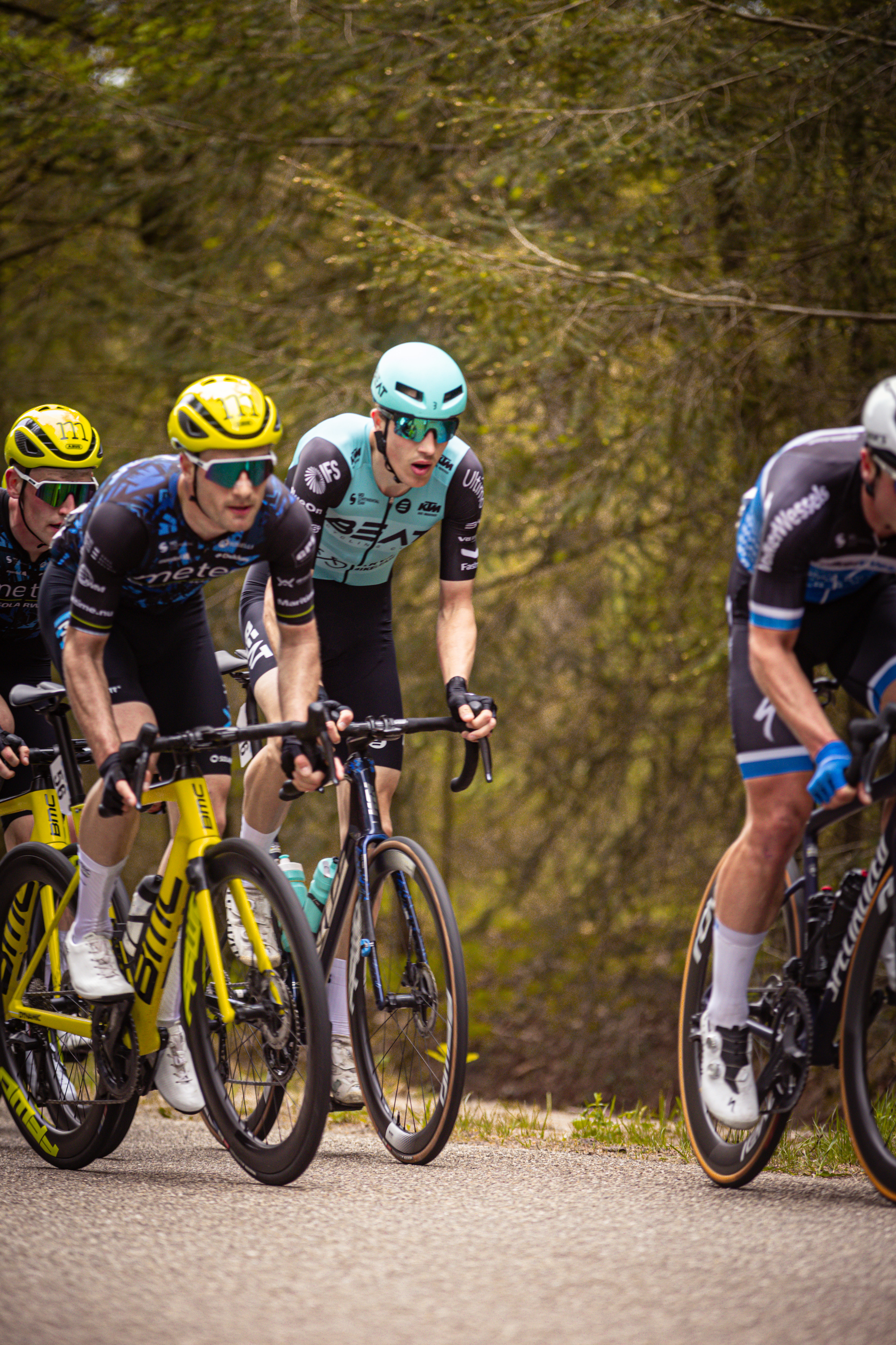 A group of men are riding bikes on a road. They have helmets and jerseys with a large number 4 on them.