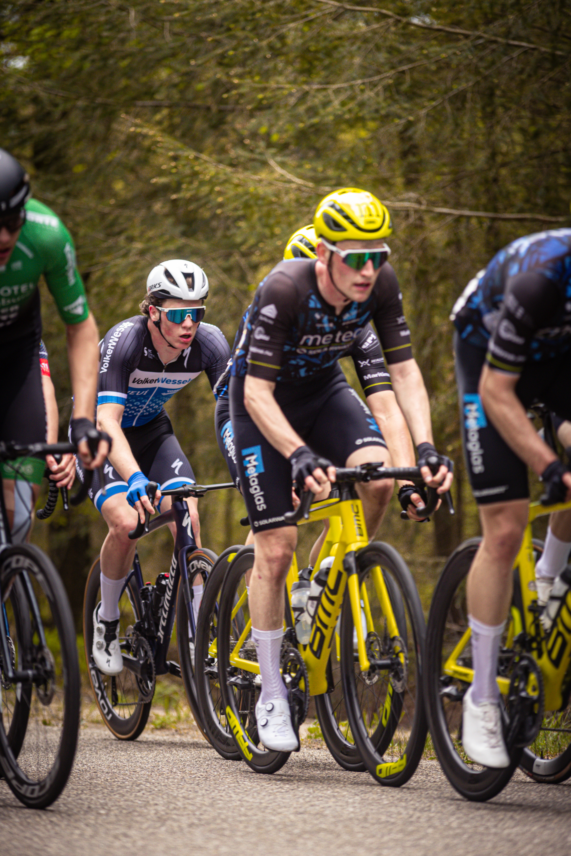 Three men riding yellow and black bikes down a road during the Ronde van Overijssel.