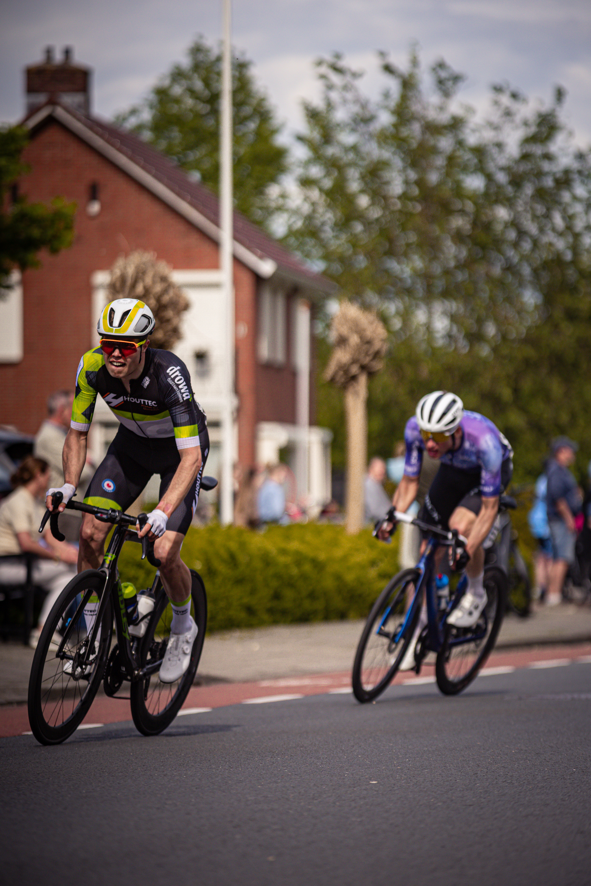 Two cyclists in a bike race with one wearing a yellow helmet and the other white helmet.