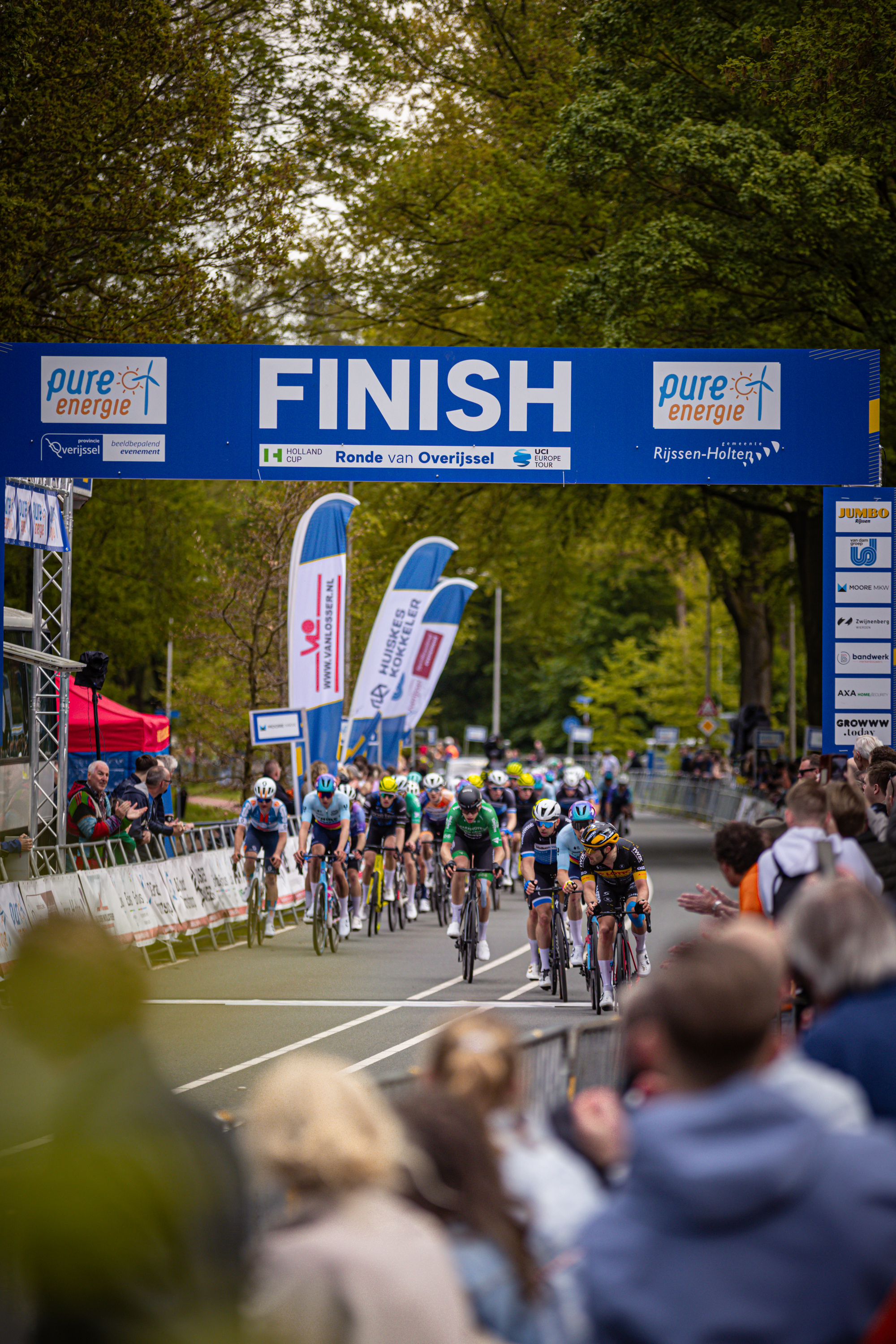 A group of cyclists race on a course under a blue sign that reads "FINISH" and "pure marathon".