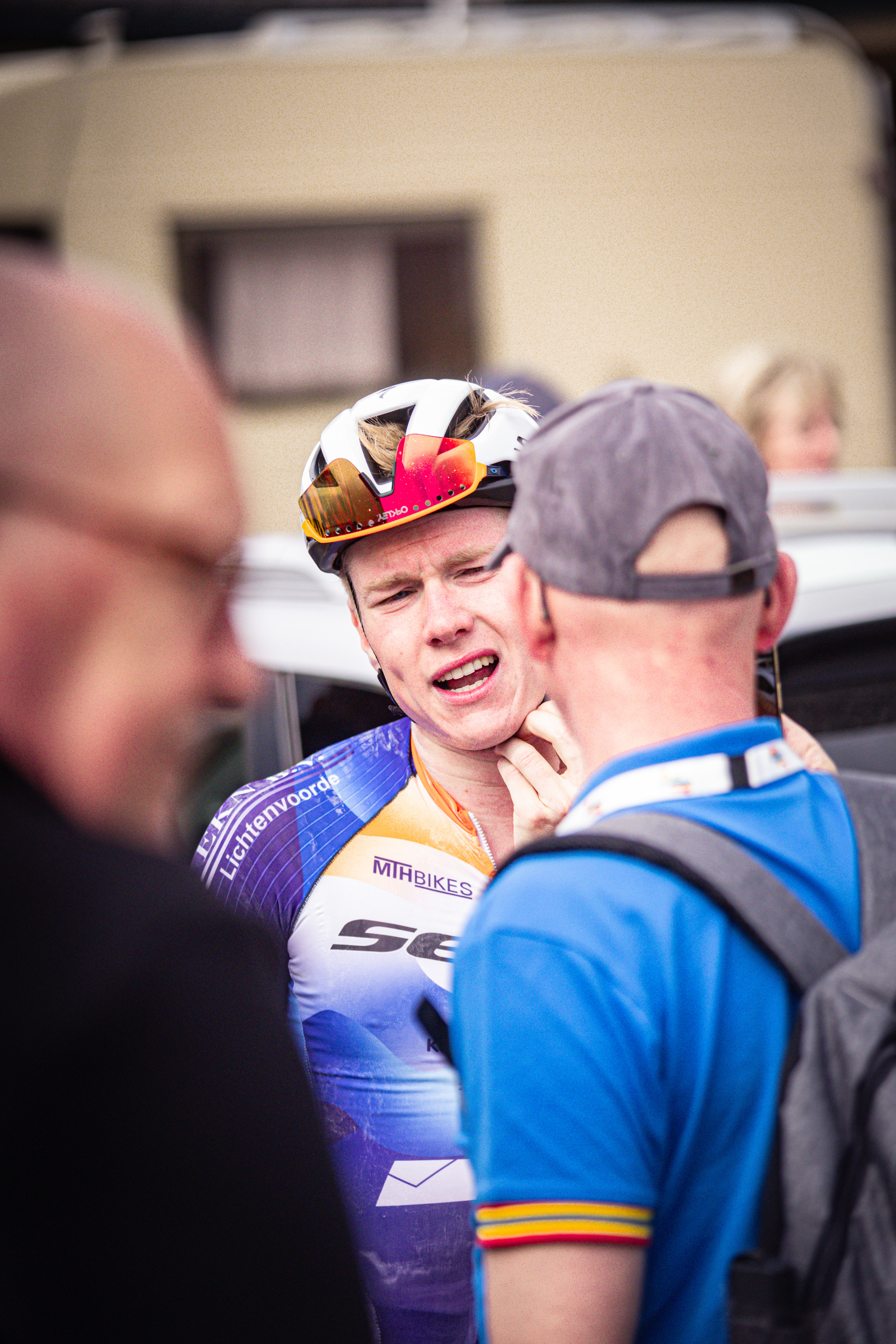 A cyclist wearing an orange and white jersey with the number 8 on it talking to another person.