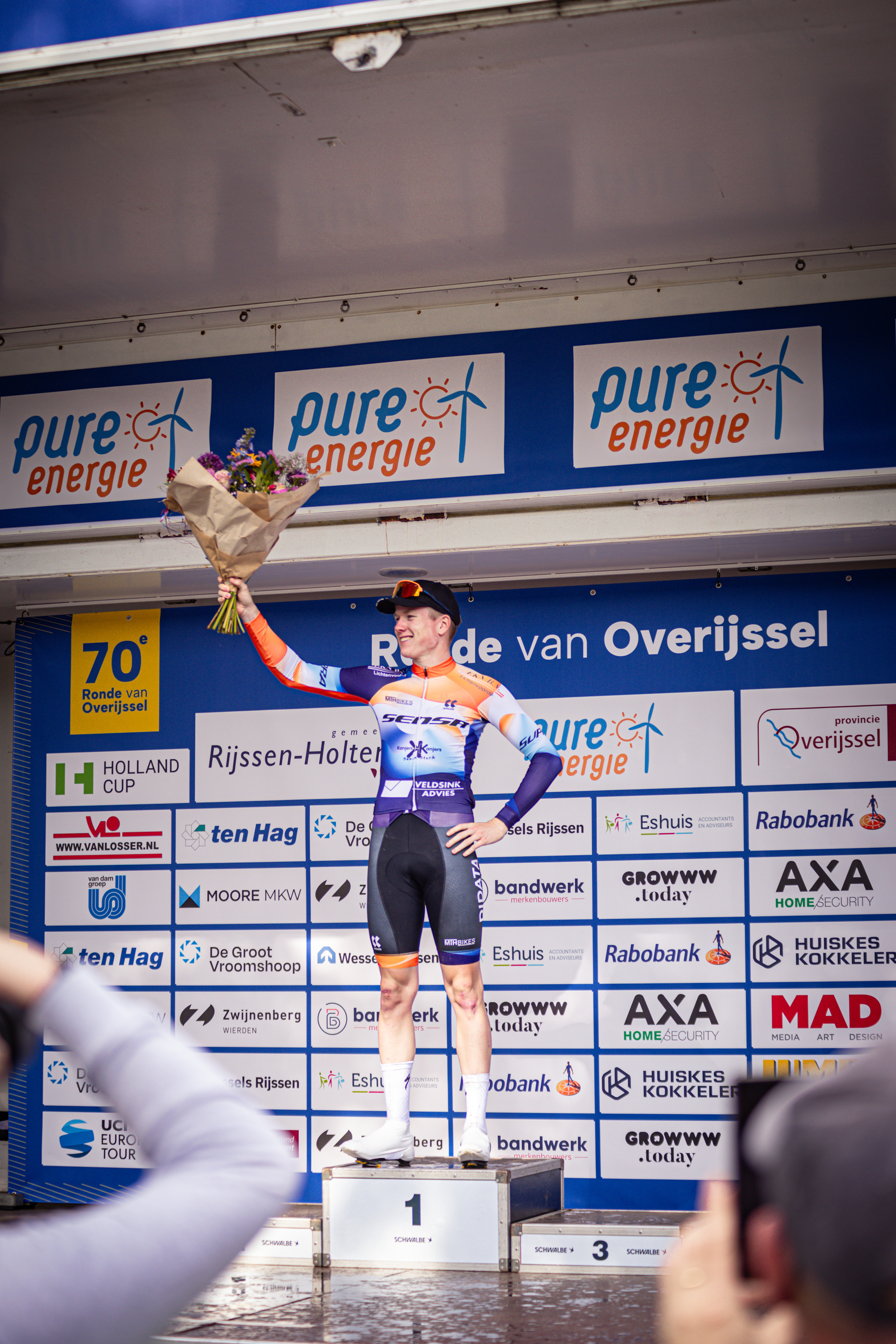 A man holding a bouquet of flowers stands on a podium at the Ronde van Overijssel.