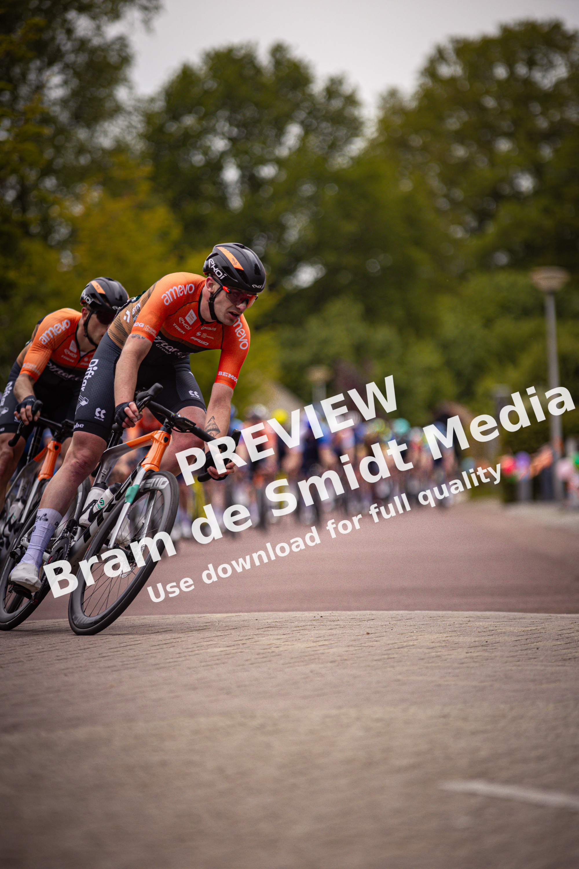 A group of cyclists wearing orange and black jerseys race down a street.