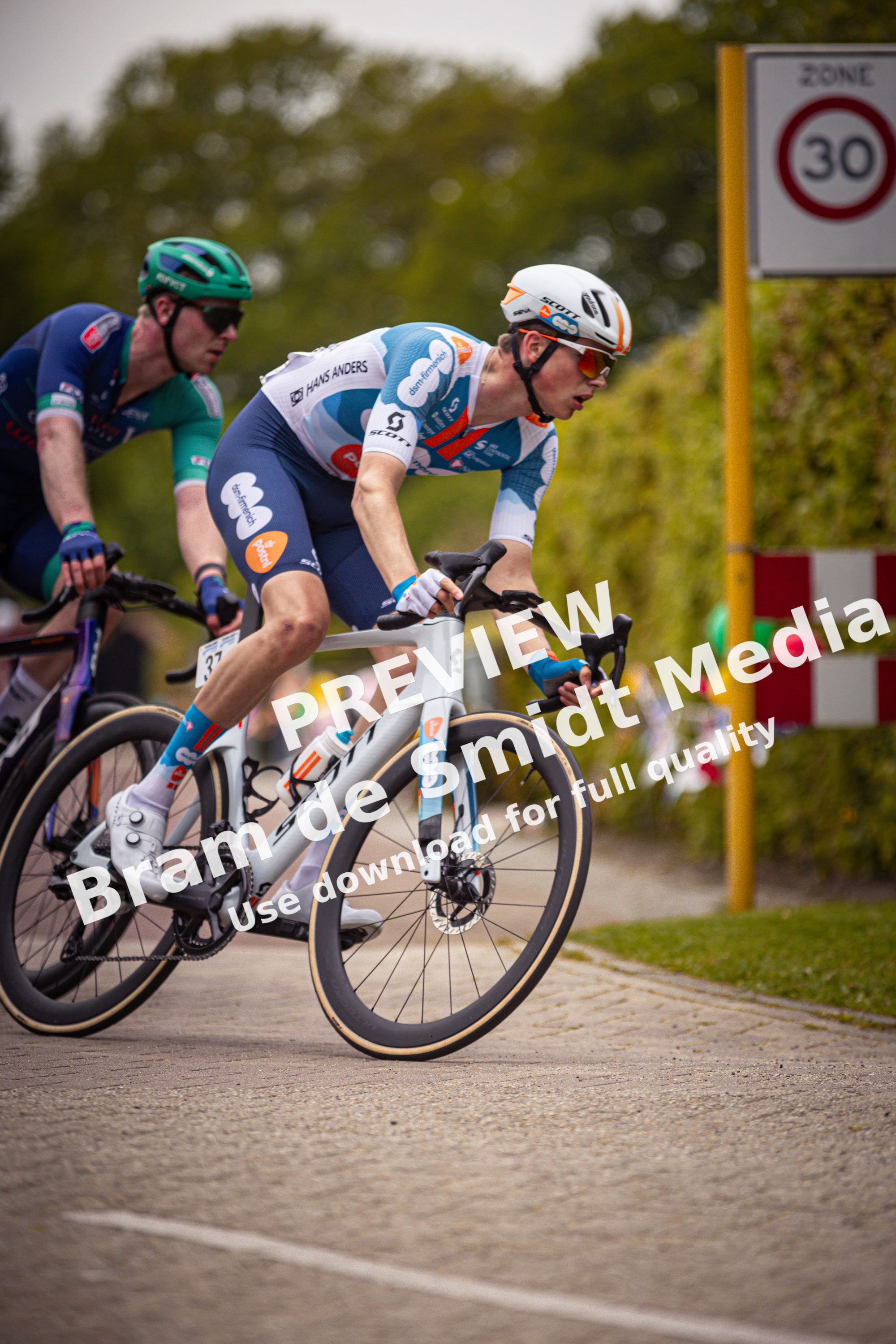 Two cyclists riding in a road with one wearing a blue and white jersey.