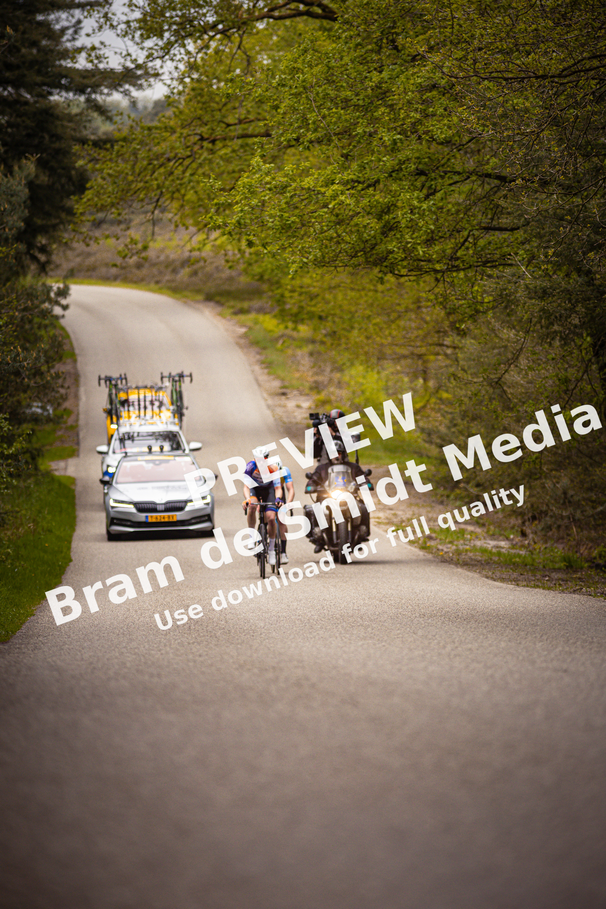 Two bikers on a road with one wearing a blue and white shirt.