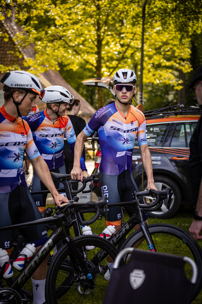 Four cyclists in colorful jerseys stand near their bikes.