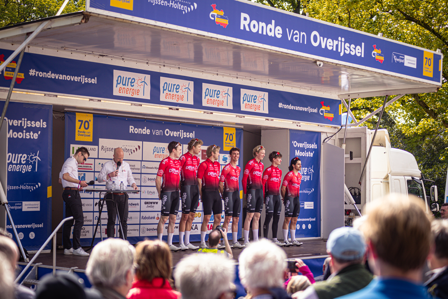 A group of men stand on a stage at Ronde van Overijssel, wearing red and white jerseys.