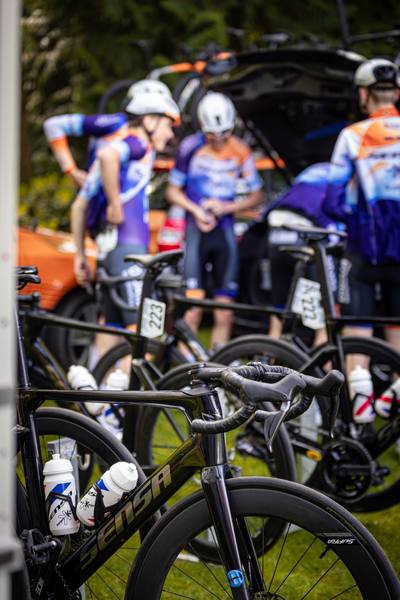 A group of cyclists standing around a car in what appears to be a parking lot.