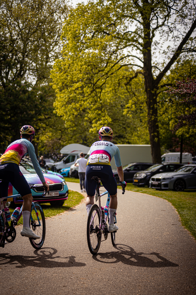 Two cyclists race down a road near cars and trees.