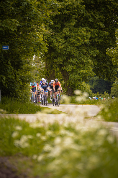 A group of cyclists riding down a street and racing in the Ronde van Overijssel.