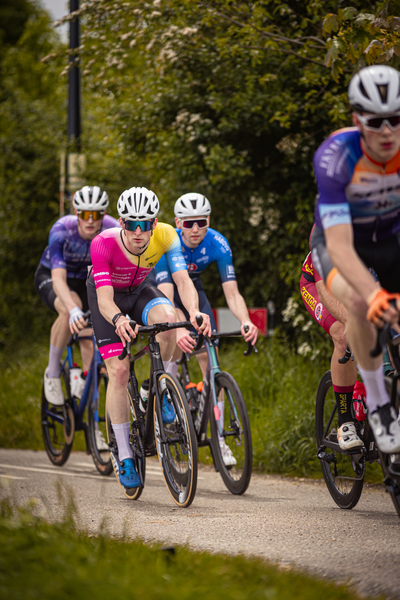 A group of cyclists are racing on a gravel road, with one man leading the pack.