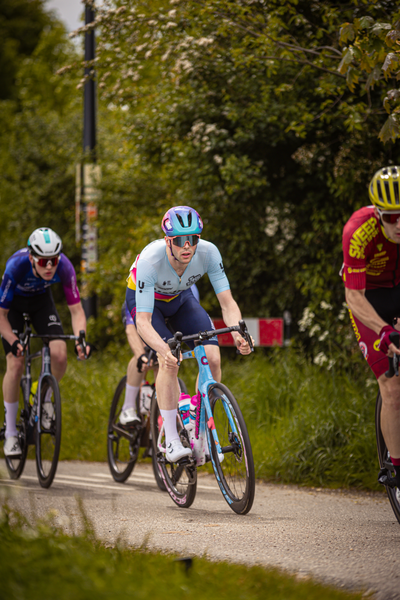 Three cyclists are riding on a road near trees and bushes.