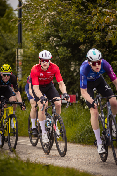 Three cyclists are racing down a street, two on black bikes and one on a yellow bike.