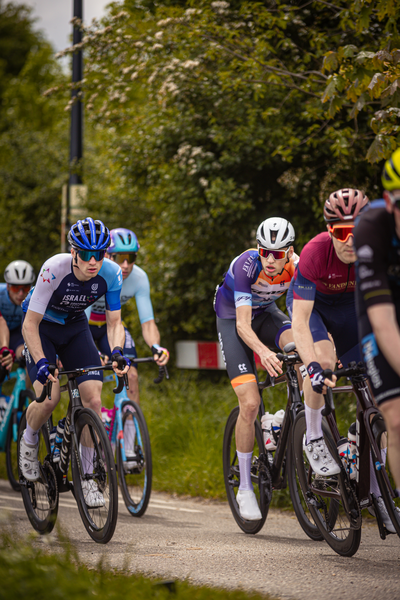 A group of cyclists on a race track with one wearing an orange and black bib.