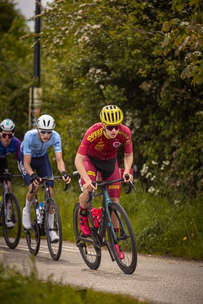 Three cyclists on a road, with the man in red wearing an Oakley helmet.