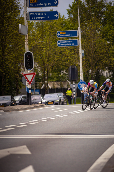 A group of cyclists race on a road with a sign for Wielrennen 6, Lijberg 15 and Aaen to the right.