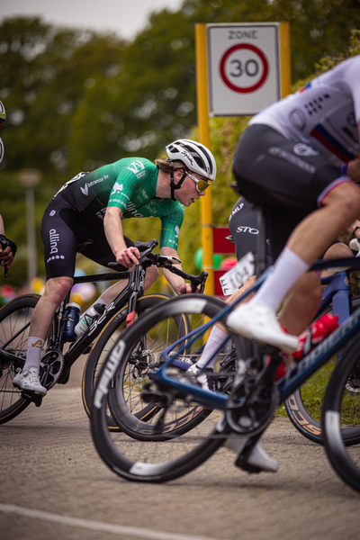 Three cyclists are riding on a road, one of which is wearing a number 20. They are in front of a sign that says "Zone".