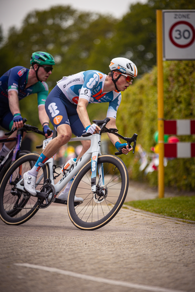 Two cyclists riding in a road with one wearing a blue and white jersey.