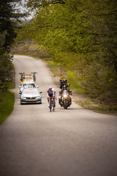 Two bikers on a road with one wearing a blue and white shirt.