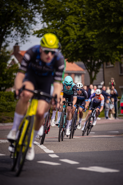 A man wearing a yellow helmet is riding on the road next to other cyclists.