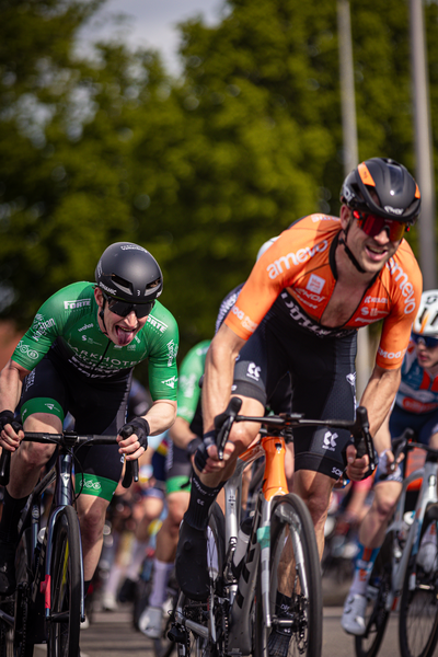 Two cyclists are competing in a bike race with the cyclist on the left leading.