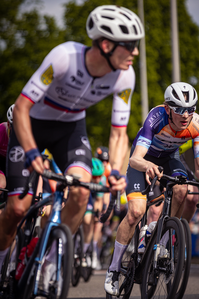 A group of cyclists are participating in a race, including one wearing a Wielrennen jersey.