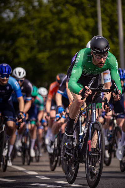 A man in a green cycling outfit is riding his bike in the street. He is sponsored by Giant and has the number 1 on his shirt.