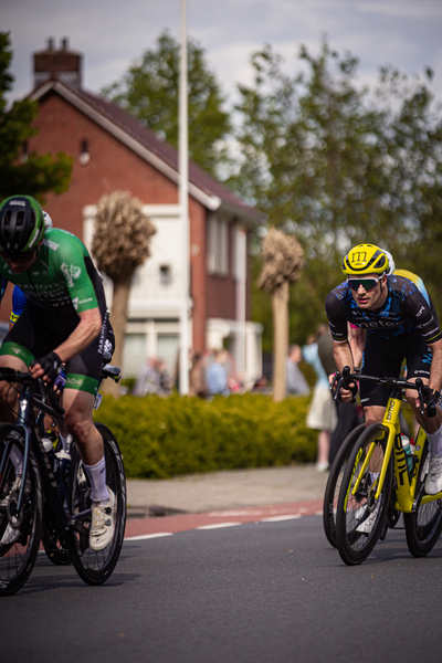 Two men are racing bicycles on a street in front of buildings.