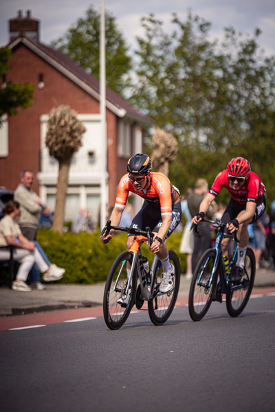 Two cyclists wearing orange and red jerseys racing on a street.