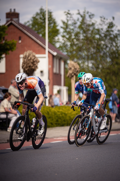 Three cyclists are riding on a street with houses in the background.