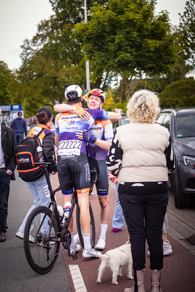 Two cyclists hug each other as they stop on the side of a road.