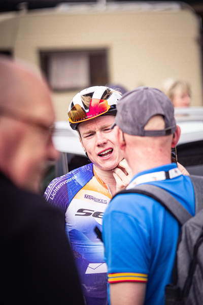 A cyclist wearing an orange and white jersey with the number 8 on it talking to another person.