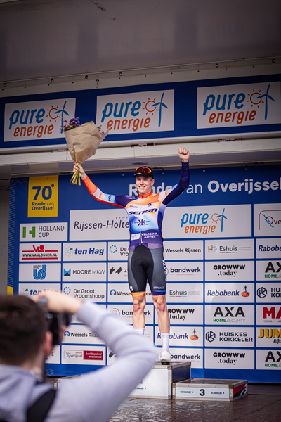 A man is holding up a bag and wearing an orange jersey.