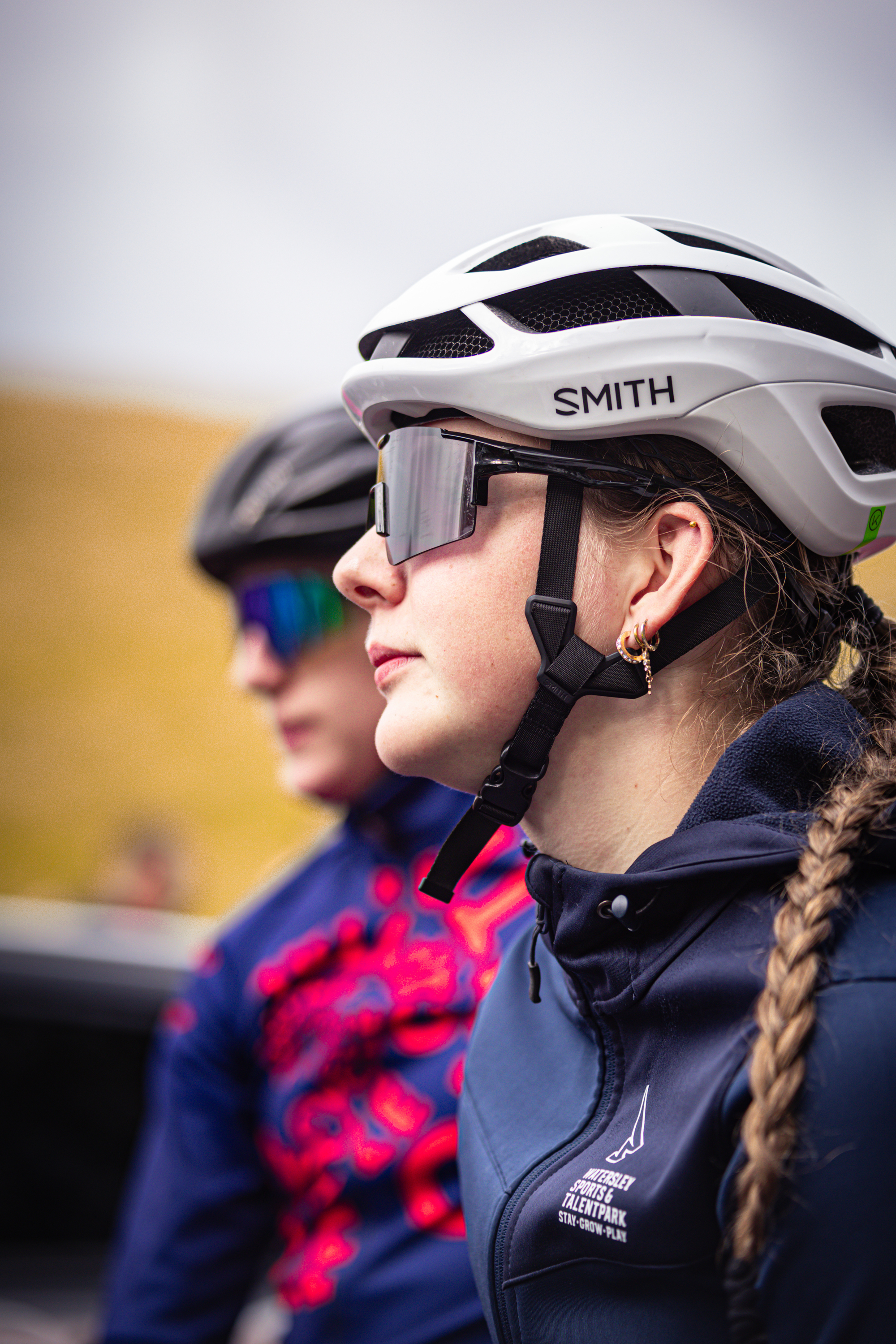 Two women wearing a helmet and goggles, with the woman in the foreground wearing sunglasses on top of her helmet.