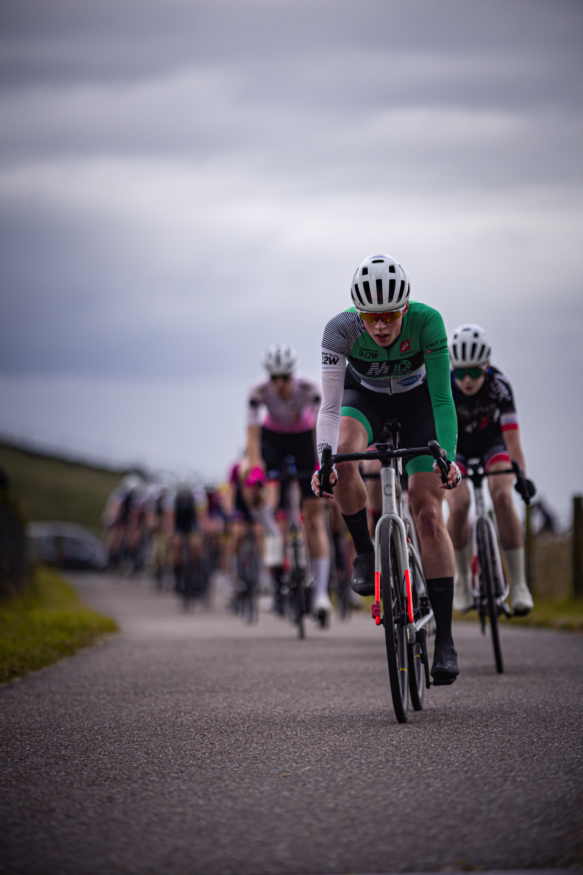 A group of cyclists race down the road, with a woman wearing an elite jersey in the lead.