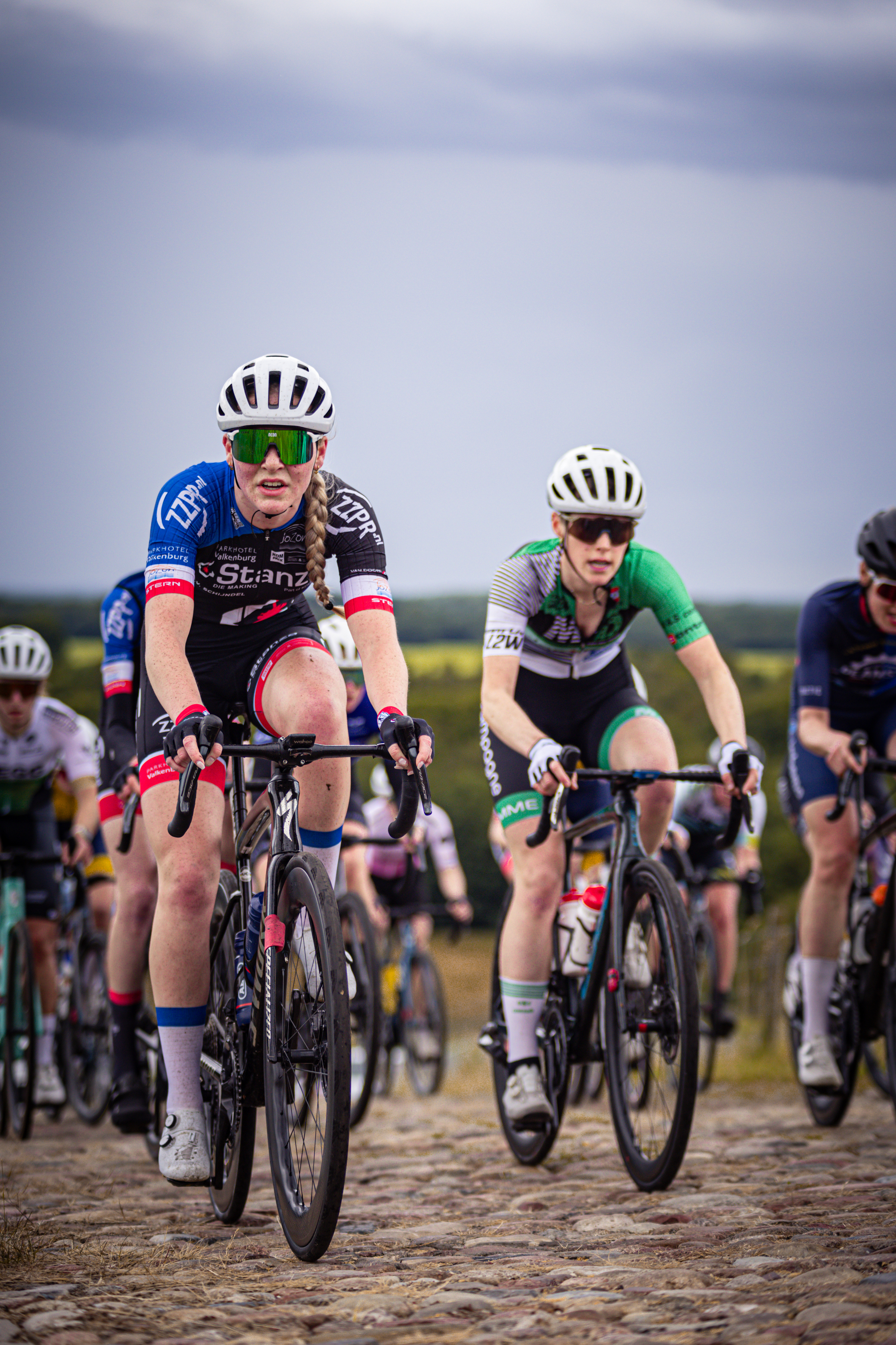 A group of cyclists are riding on a cobblestone road with the words Nederlands Kampioenschap on their jerseys.