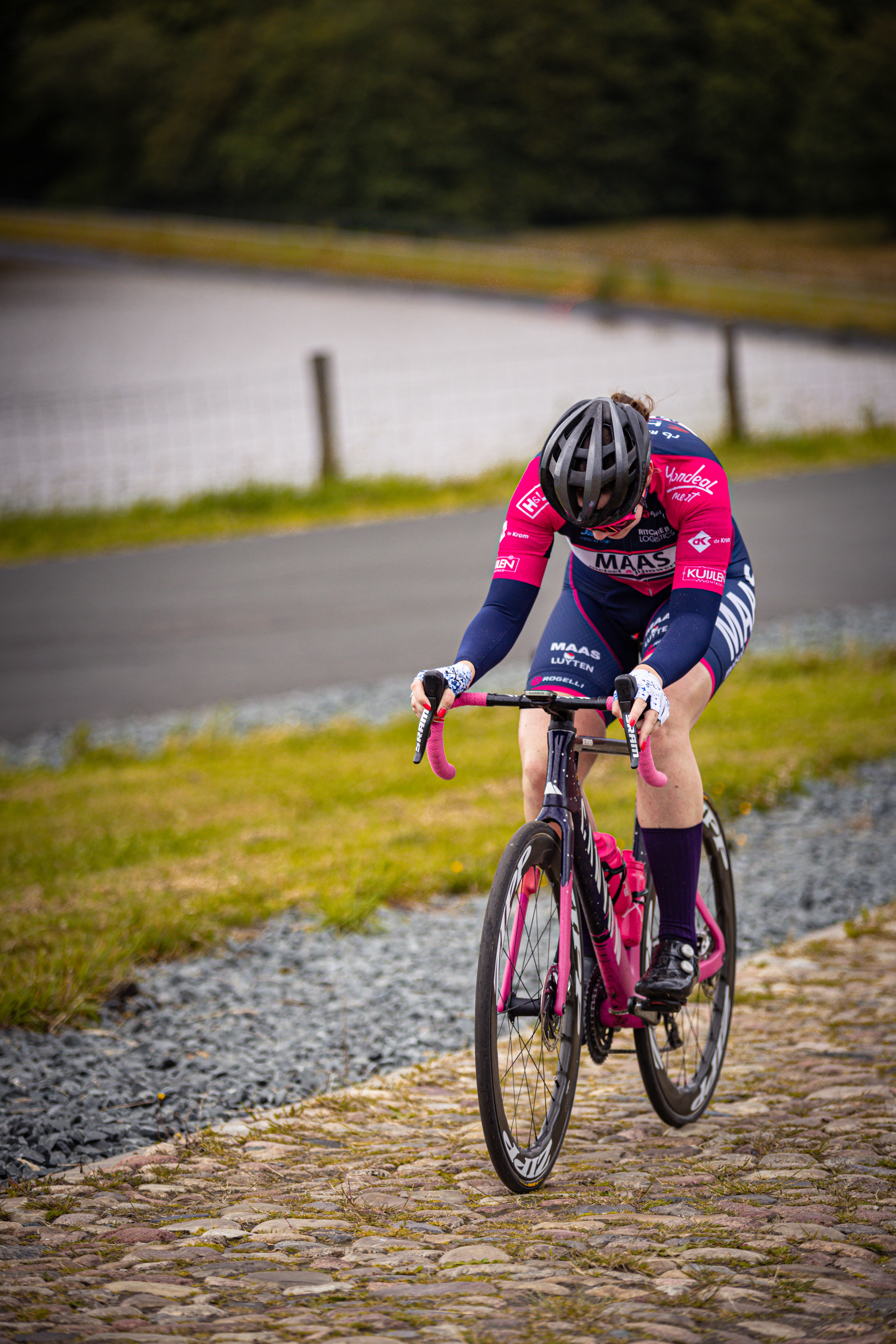 A woman in a pink jersey is riding her bike on a cobblestone road.