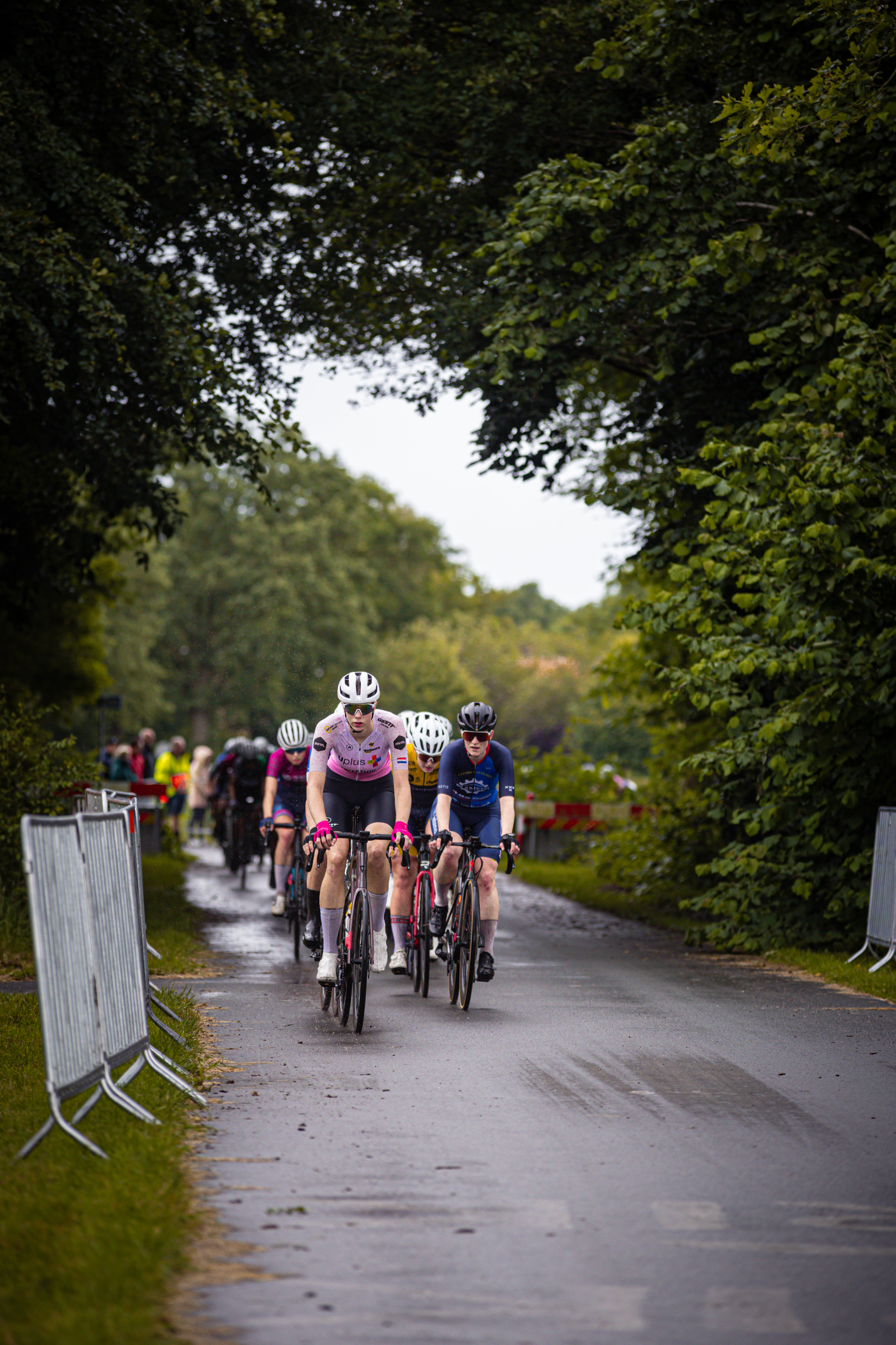 Women riding their bikes down the road, one woman wearing a purple and white jersey.