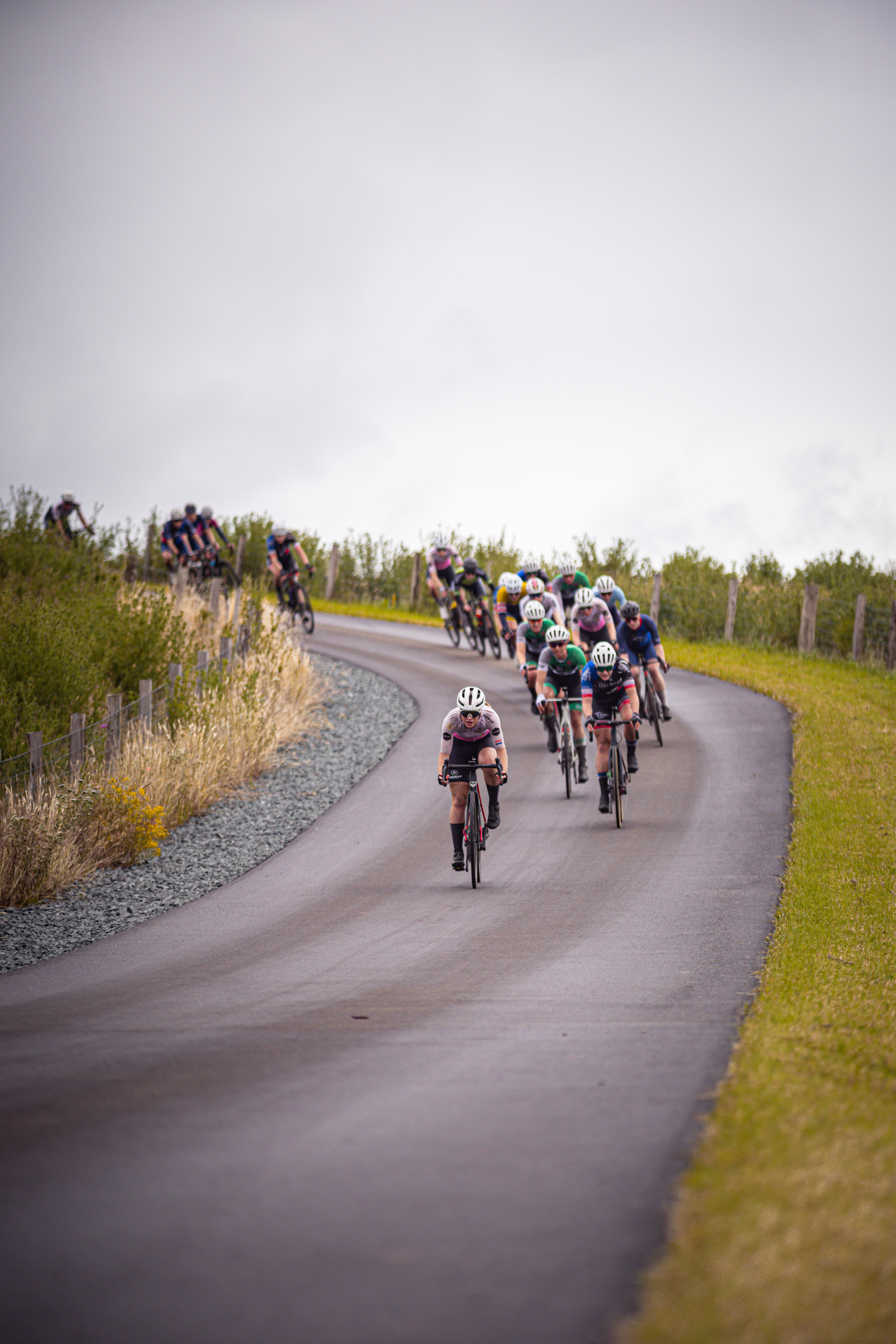 A group of cyclists are riding on a road, some are wearing helmets.