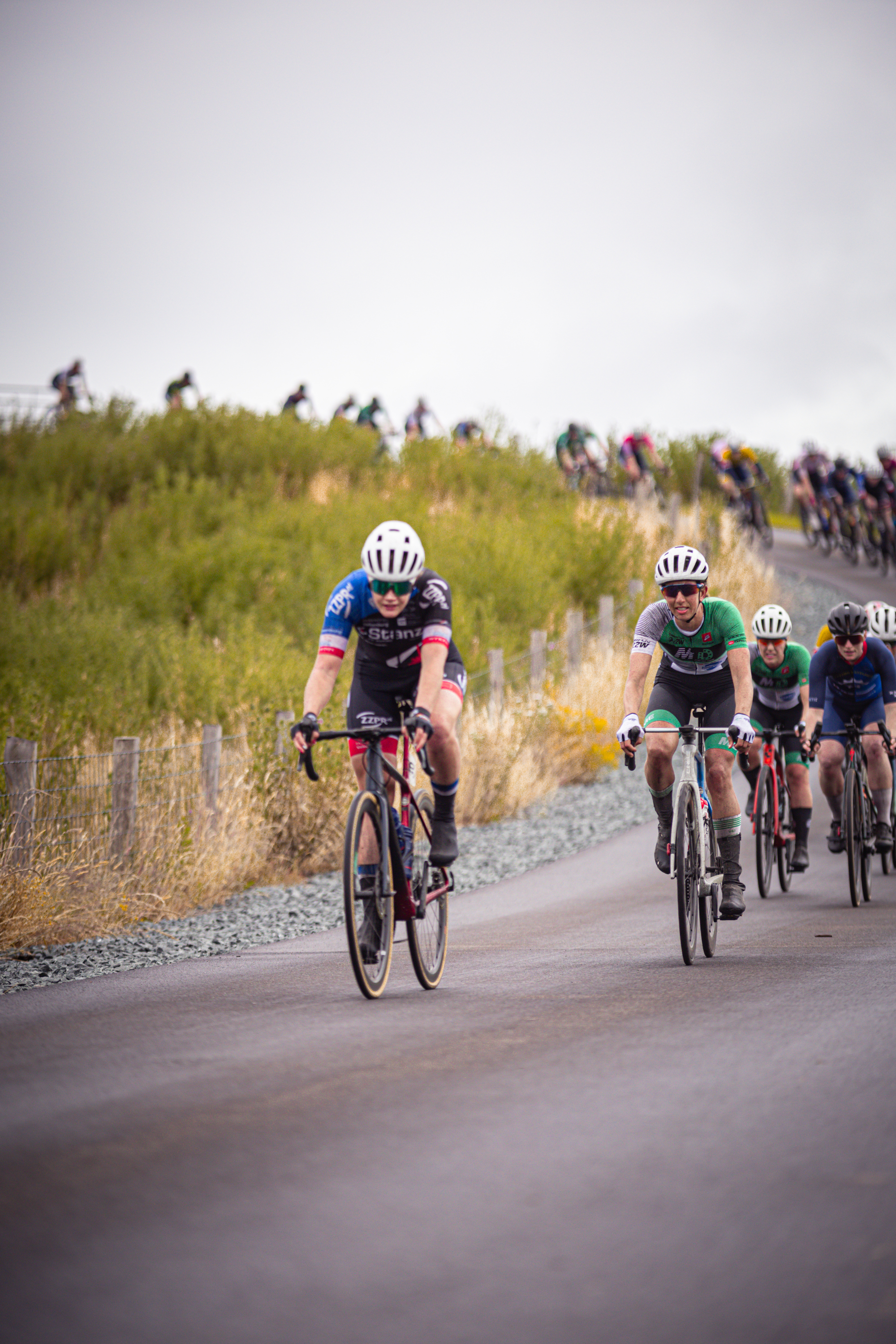 A group of cyclists compete in a race, sponsored by Nederlands Kampioenschap.